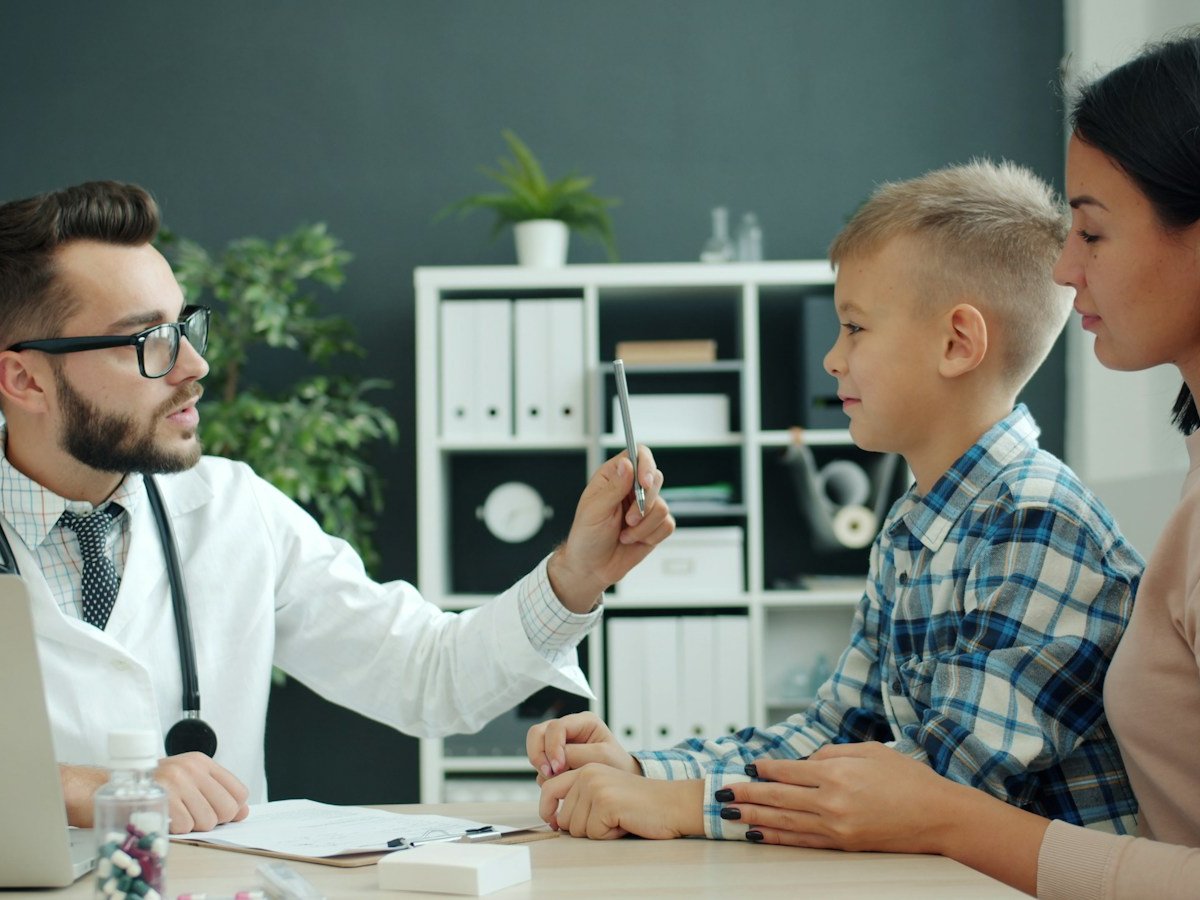 Doctor gently examining a young child during a pediatric consultation with his mother present in a warm clinical setting